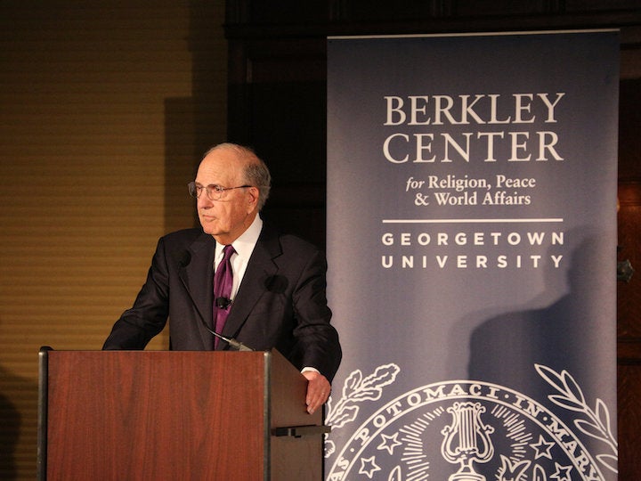 Picture of Senator George Mitchell at a podium giving a keynote in front of a rectangular sign with the Berkley Center's name and university logo on it