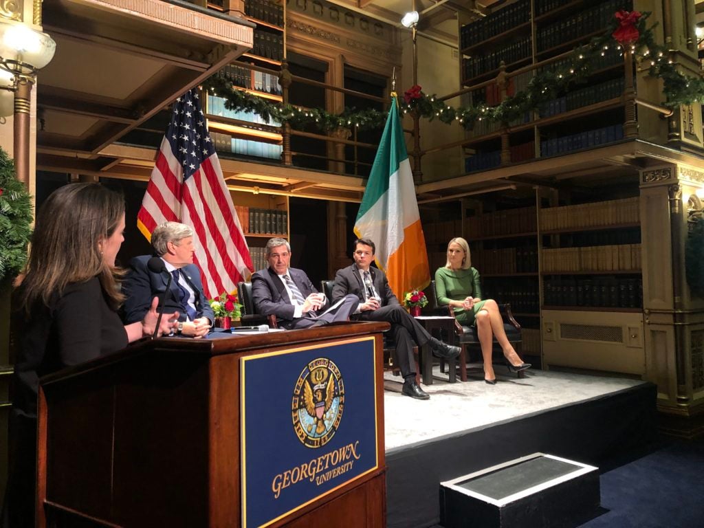 Four panelists sit on stage in front of the Irish and American flags