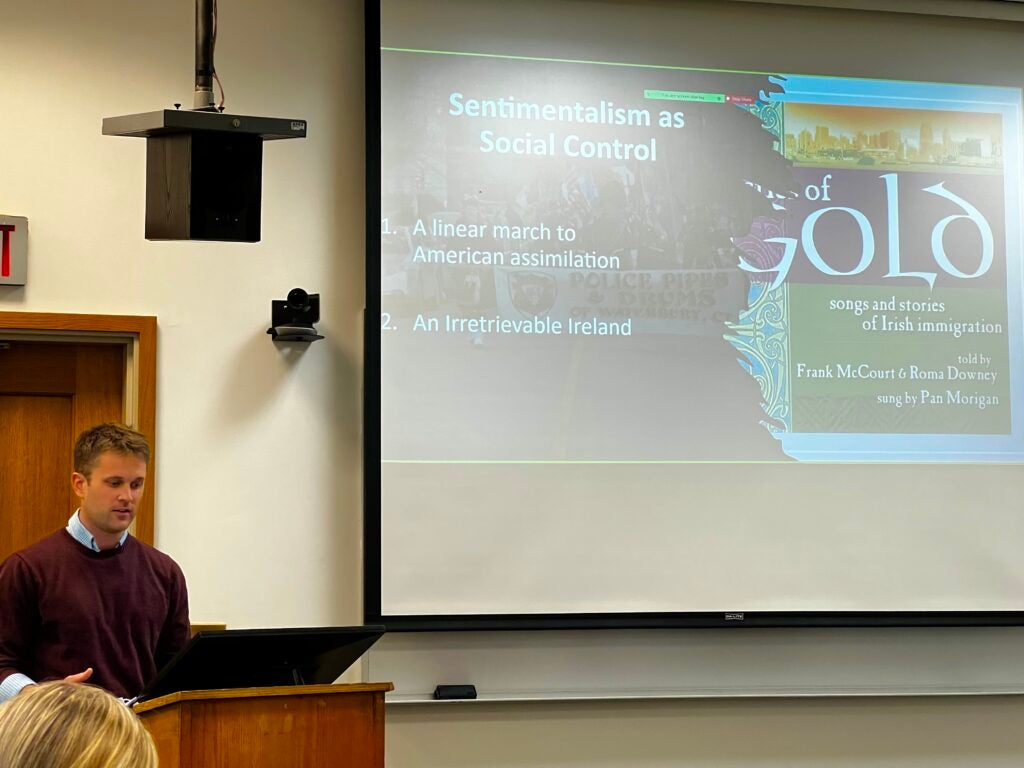 Casey Donahue stands behind a podium. A powerpoint slide reading "Sentimentalism as Social Control" is displayed beside him.
