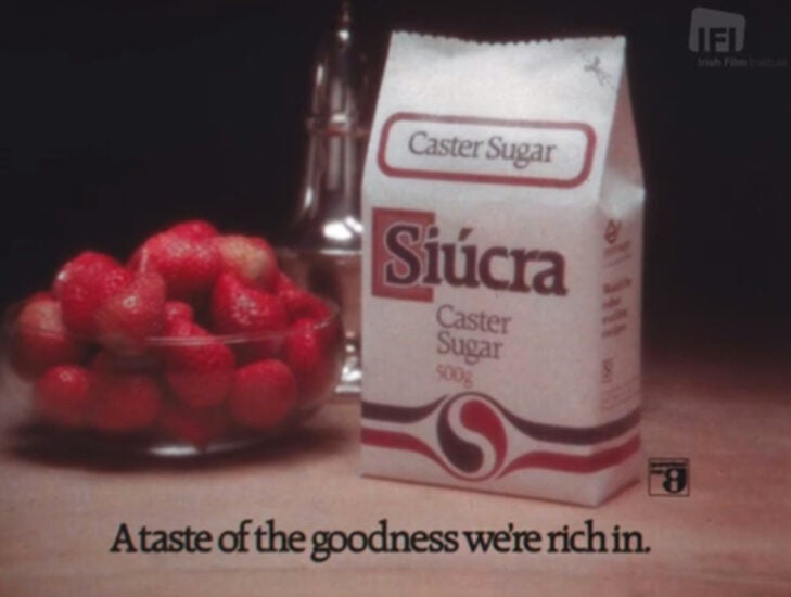 A vintage-looking ad depicting a bowl of strawberries next to a white paper bag of sugar. It reads "A taste of the goodness we're rich in"