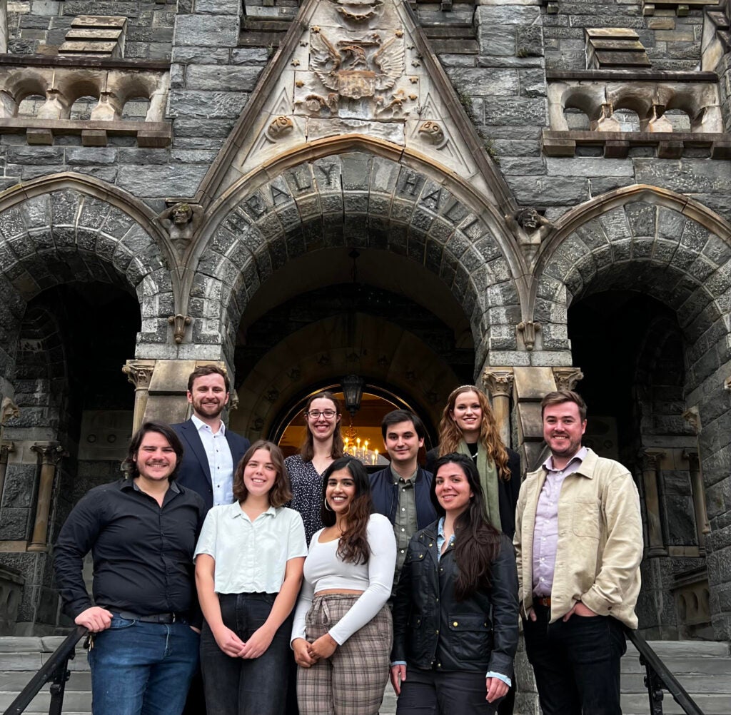 nine students standing on the steps outside of Healy Hall on Georgetown main campus, facing the camera and smiling.