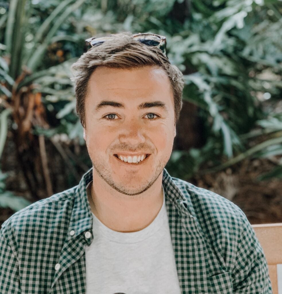 Patrick McSweeney (student) smiles into the camera against a backdrop of greenery.
