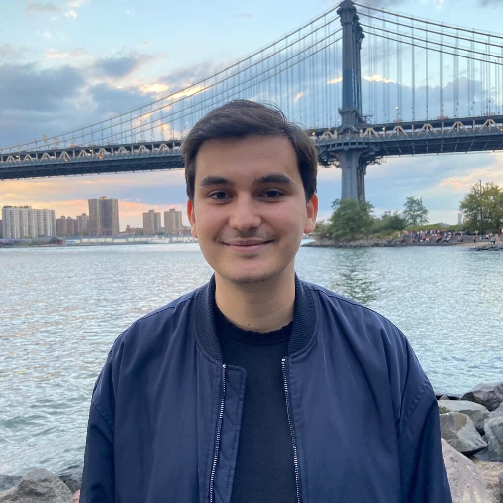 Louis (student) smiles into the camera while standing in front of a bridge and body of water.