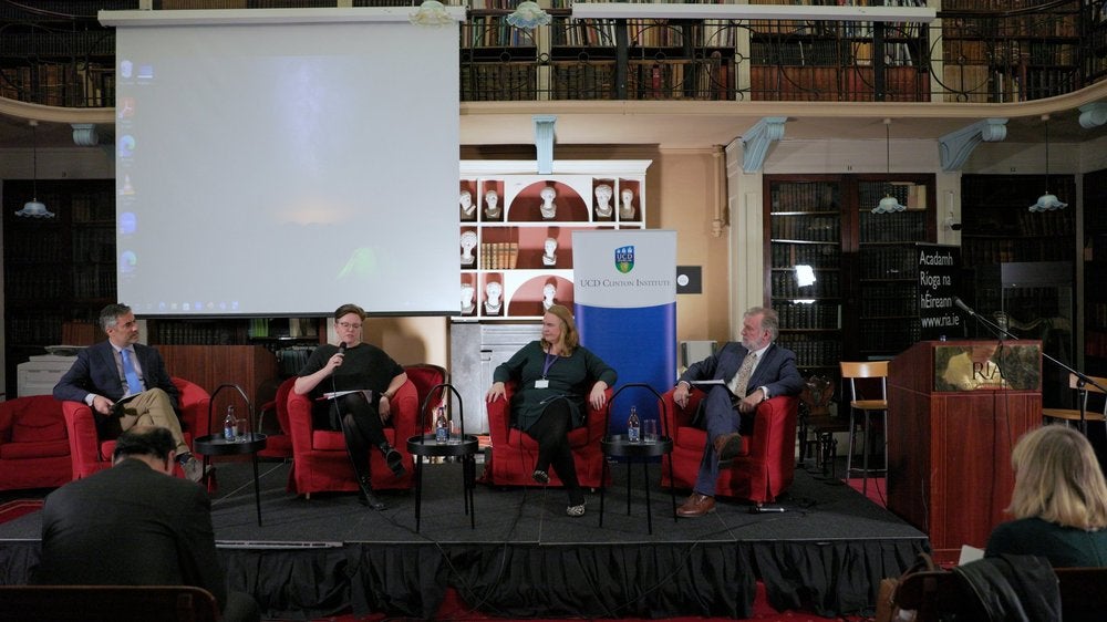 Prof. Cóilín Parsons (Georgetown University), Prof. Belinda McKeon (Author, Maynooth University), Prof Miriam Nyhan Grey (New York University), Prof. Liam Kennedy (UCD Clinton Institute) sitting on a stage in red armchairs.

