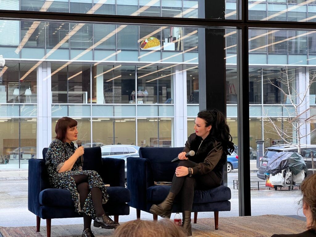 Sinead Gleeson and Aideen Barry sit on stage against a glass wall overlooking the street in Washington DC