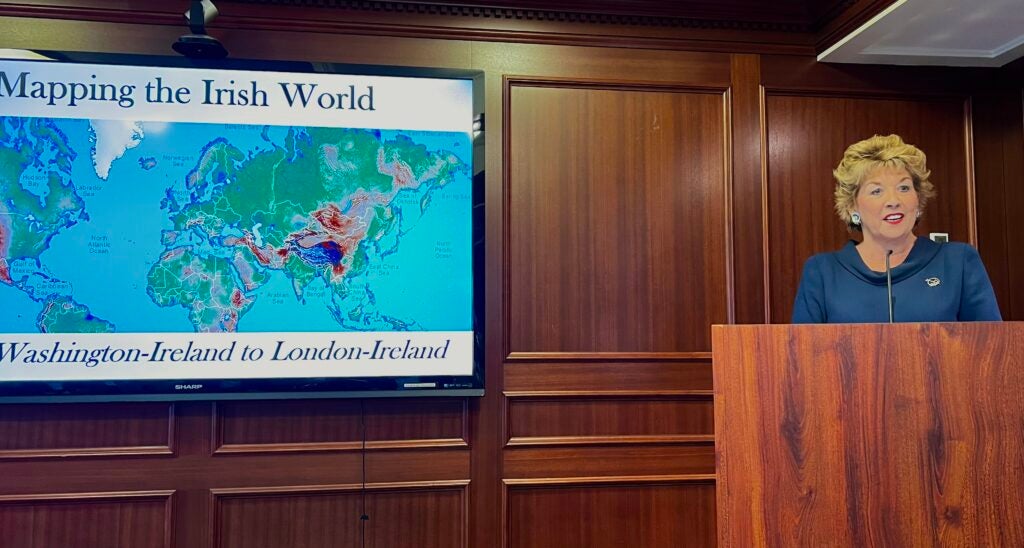 Ambassador H.E. Geraldine Byrne-Nason stands at a podium and speaks in front of a screen reading "Mapping the Irish World"