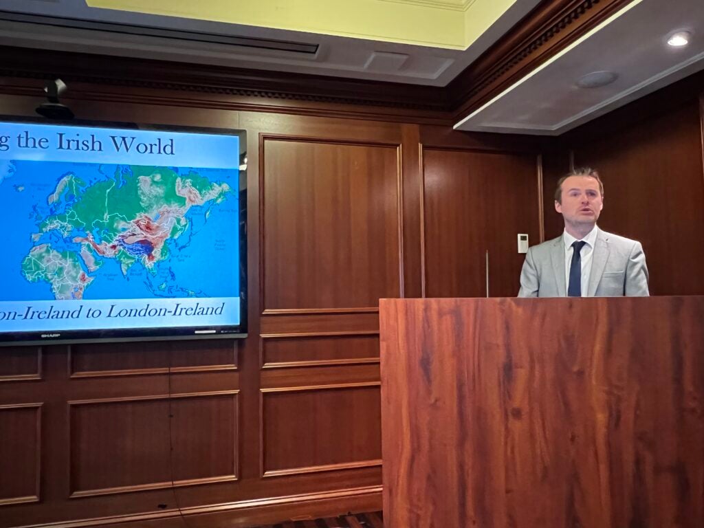 Dr. Darragh Gannon speaks at a podium in front of a screen reading "Mapping the Irish World"