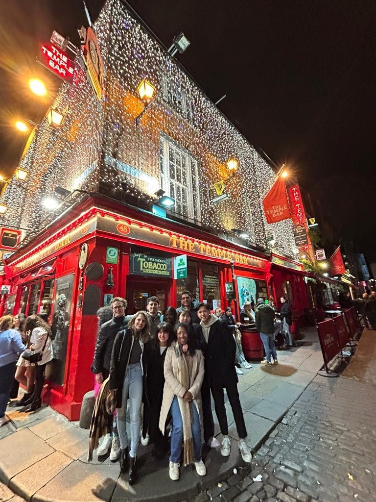 a group of students stands in front of a lit-up building with sign "The Temple Bar"