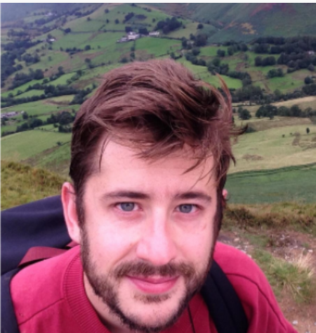 Image is a headshot of Dr. O'Hanlon. He wears a red sweatshirt while looking at the camera and has a pastoral scene in the background.