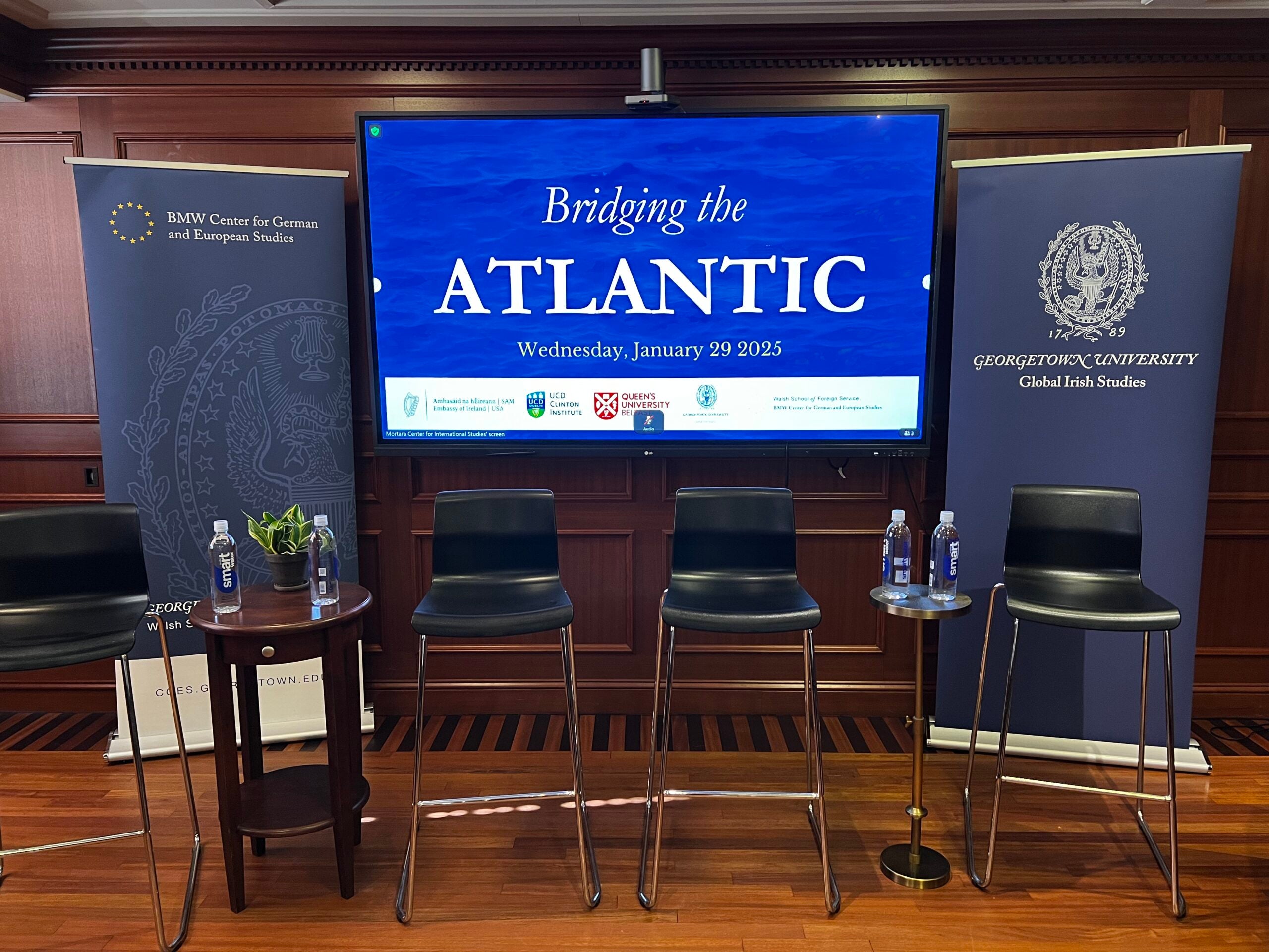 Three empty chairs in room with background of screen reading "Bridging the Atlantic" with two banners on either side